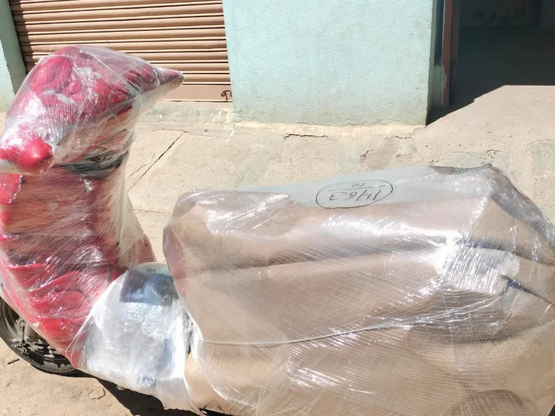 Red bubble-wrapped scooter resting securely on roadside pavement before loading