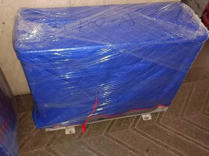 Compact sofa unit tightly wrapped in bright blue stretch wrap standing indoors